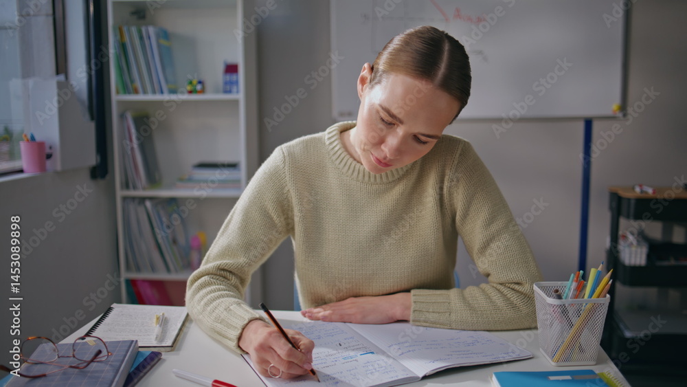 Focused lady checking homework at class room closeup. Teacher putting marks
