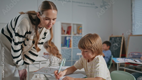 Teacher kid having lesson in classroom closeup. Woman helping pupil with test