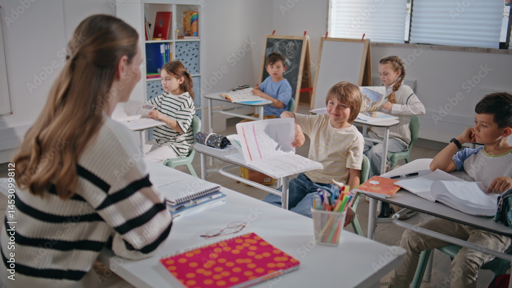Smiling teacher asking questions to kids in elementary school class room closeup