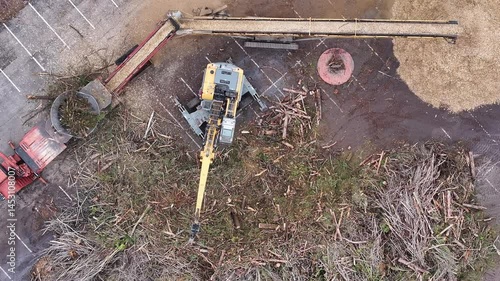 Wallpaper Mural shot looking straight down on a parking-lot staging area where an excavator feeds storm-felled tree debris into a tub grinder, converting tangled branches into a swirling mound of fresh wood chips Torontodigital.ca