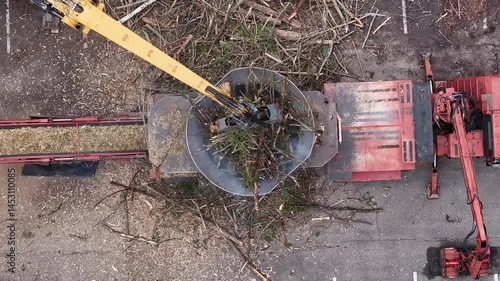 Wallpaper Mural Aerial drone view of a powerful tub grinder in action: an excavator arm feeds storm-felled branches into the circular hopper while a conveyor belt expels shredded wood chips onto a growing pile below. Torontodigital.ca