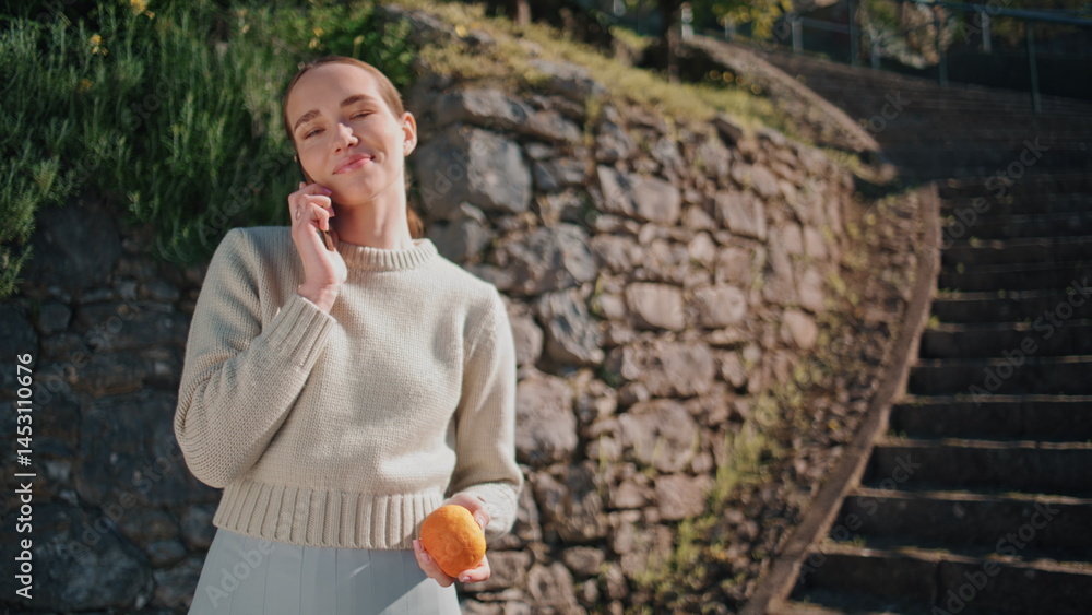 Cute model talking smartphone at greenery park closeup. Woman holding orange