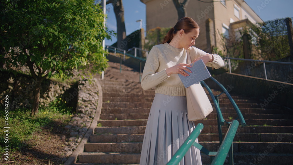 Young teacher checking notebook at sunlight staircase. Woman enjoying break