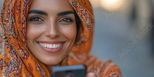 Obraz na płótnie Happy woman taking a selfie with her cellphone. She is wearing a colorful hijab and has well-done makeup. w salonie