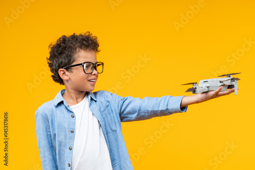 Studio shot of casually dressed African American schoolboy posing over yellow background with generic design drone in his hand, science, technology, modern education concept