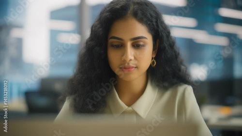 Young professional it specialist latin hispanic business lady working on laptop pc sitting at desk in modern office space. 30s middle eastern indian woman using computer technology app for work