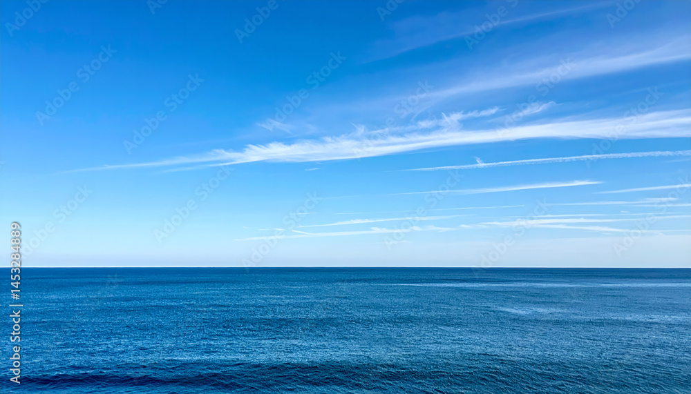 Obraz premium Calm Blue Ocean Meets a Bright Blue Sky with Wispy Clouds