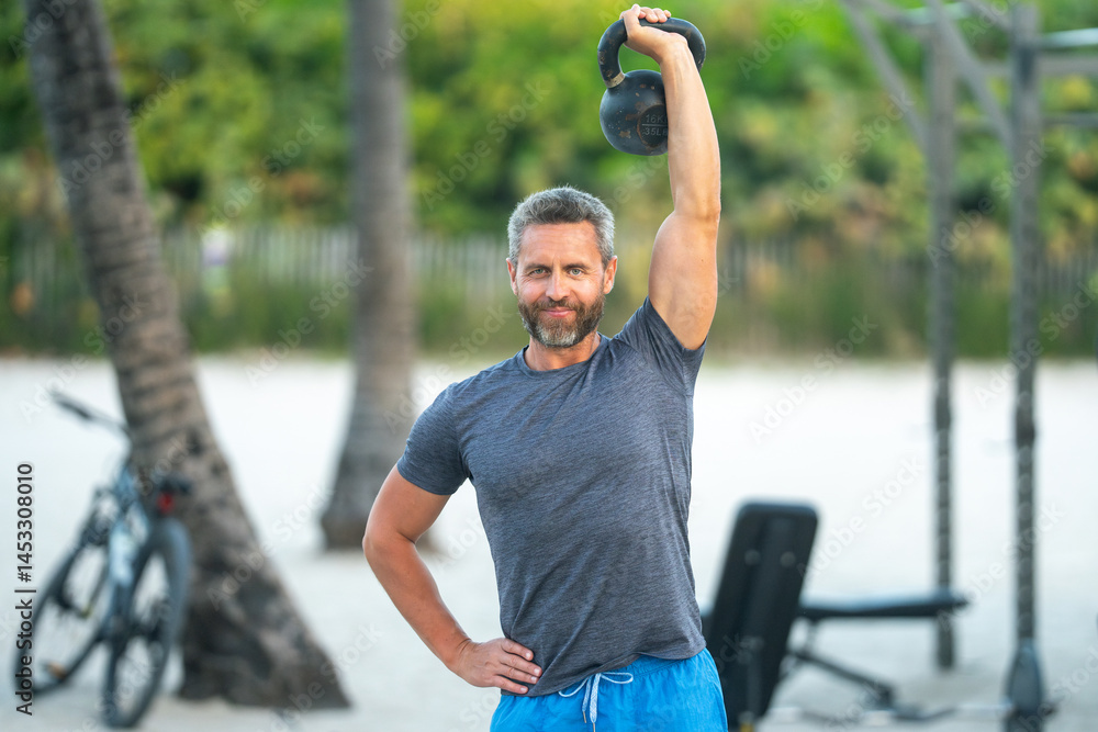 Fototapeta premium Outdoor fitness training. Sporty and muscular male working out. Beach workout. Fit man training with kettlebell. Sport man kettlebell exercises. Muscular man doing kettlebell. Kettlebell training.