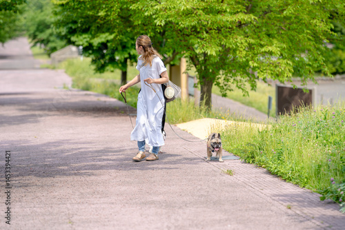 Obraz na płótnie On a summer morning in a park with blooming hydrangeas, a Japanese woman in her 30s walks two French Bulldogs. Surrounded by flowers and trees, they stroll along quiet paths under soft morning light. w salonie