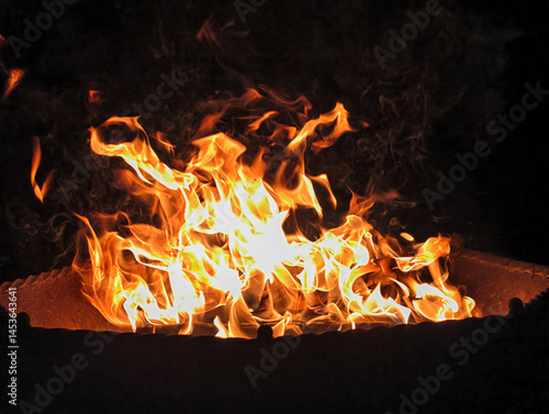 Night photo of a bonfire in an iron fire bowl. Photography of flame of burning wood on black background.