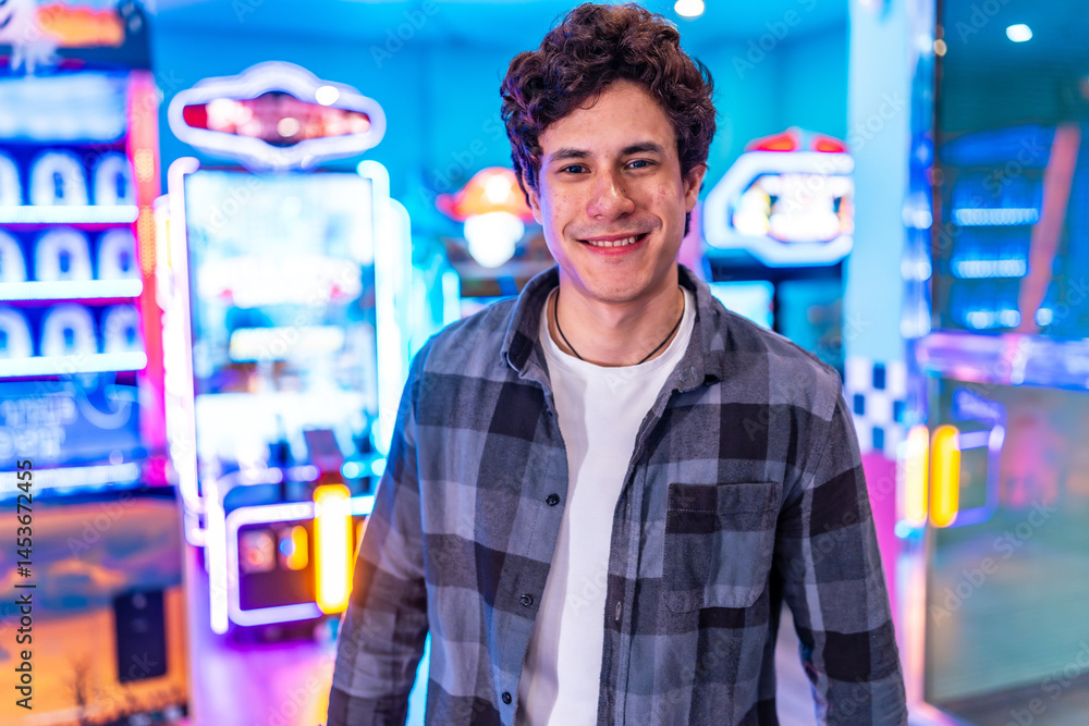 Young man smiling in a colorful arcade setting with claw machines and games