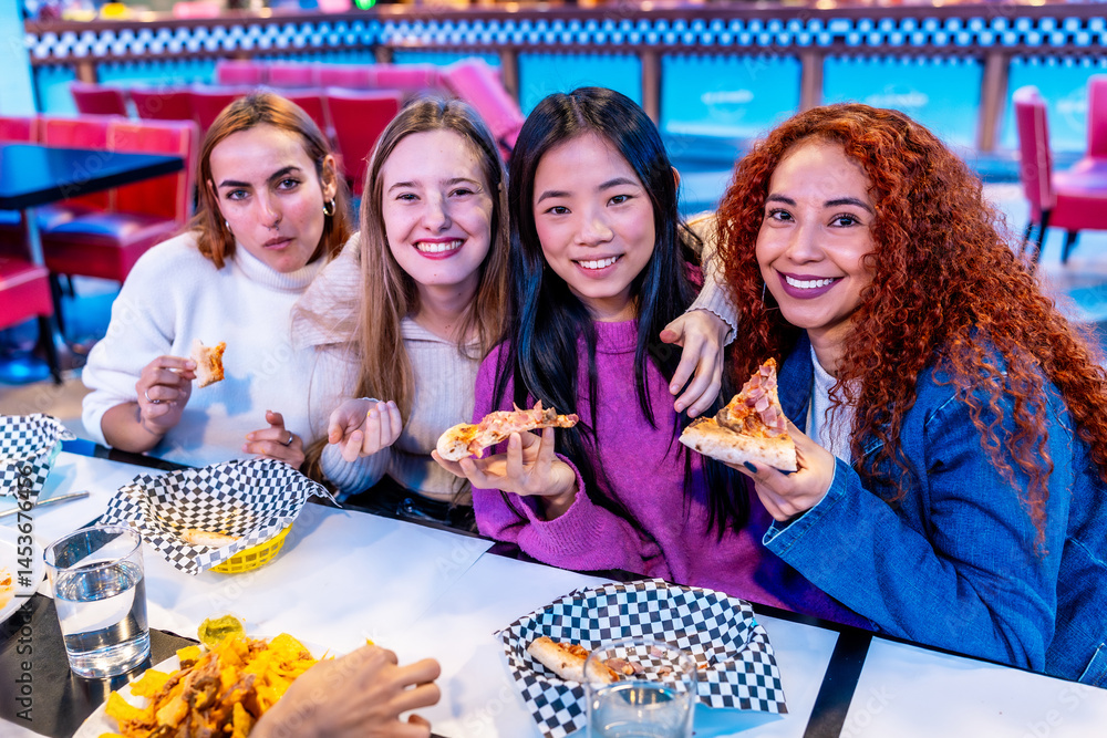 Cheerful multiethnic female friends enjoying pizza at restaurant table