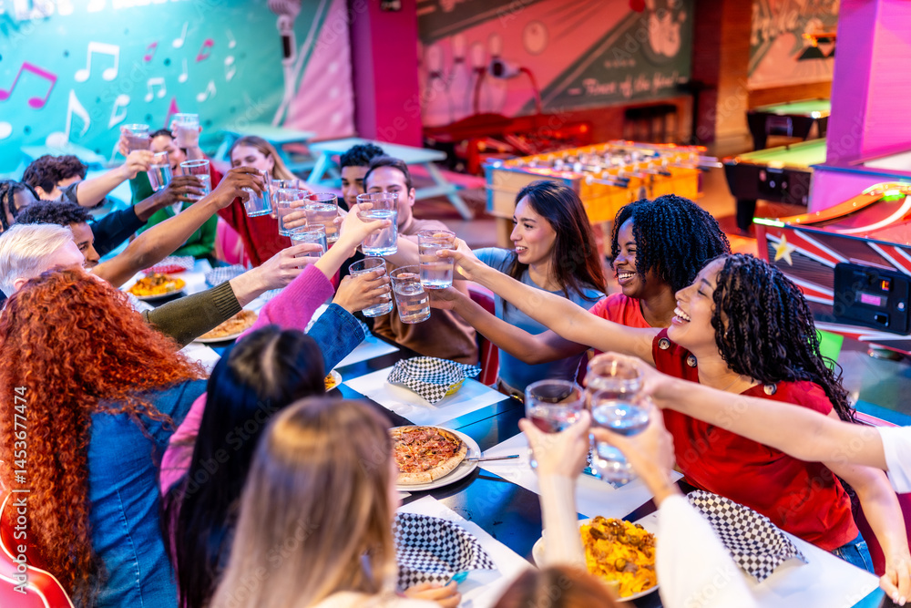 Happy multiethnic friends toasting drinks at bowling alley restaurant