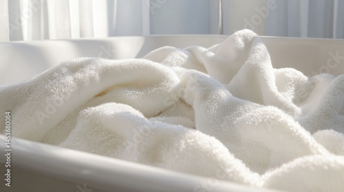 Close-up of a clean white fluffy towel folded on a bathroom or spa linen shelf with natural daylight illuminating the soft textured surface and cozy atmosphere