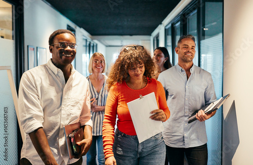 Diverse group of smiling professionals walking through modern office hallway. Energetic mood, casual business attire, teamwork vibe