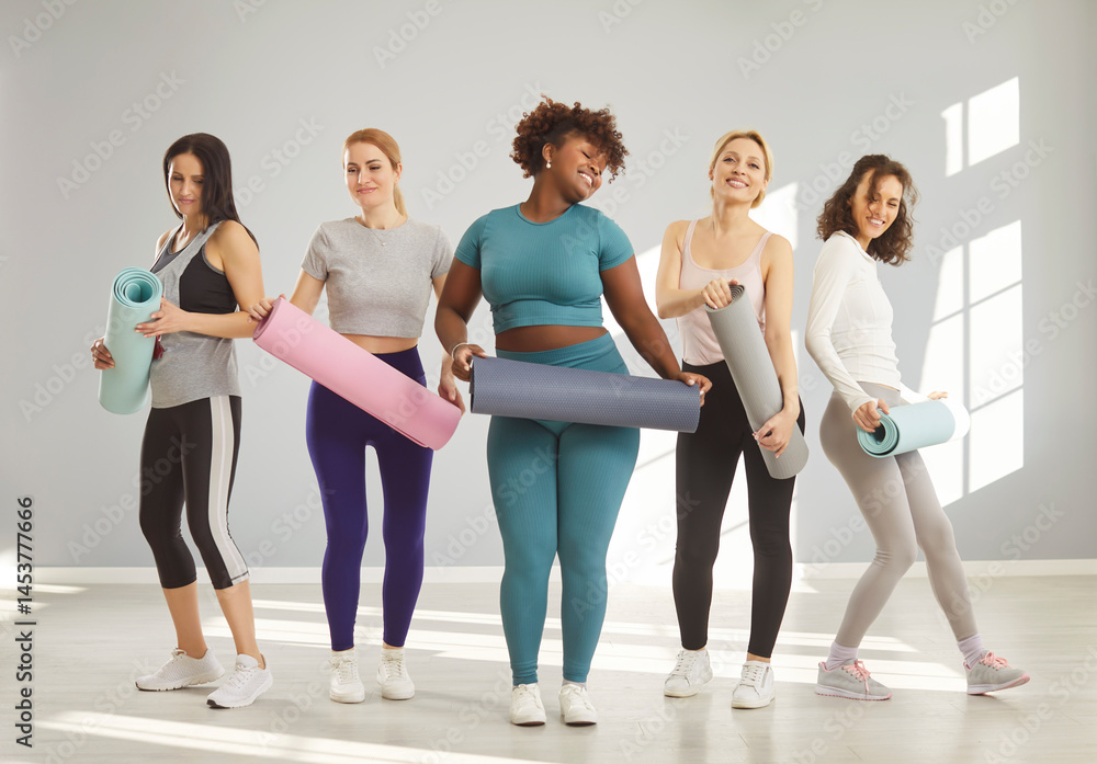 Fototapeta premium Sporty diverse women pose in full length with fitness mats prrepare for fitness training lead active healthy lifestyle smile happily. Woman and her friends rest from physical activity recover strength