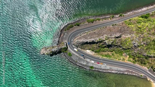 Dramatic overhead view of Maconde coastal road curving around cliffs as emerald ocean waves crash below in southern Mauritius