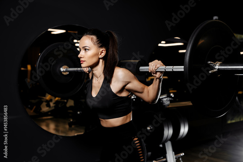 Close-up photo of confident woman doing squats exercises with heavy barbell in the gym