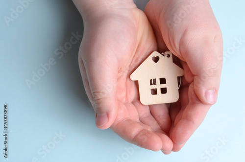A wooden keychain in the shape of a house lies in the hands. Blue background.