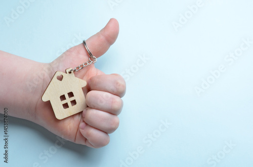 Wooden keychain in the shape of a house in hands. Close-up. Blue background.