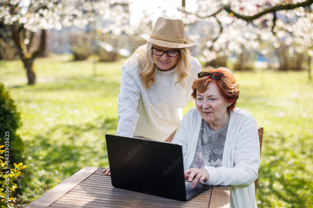 Happy moment of smiling woman with her senior mother while watching laptop screen outdoors Happy moment of smiling woman with her senior mother while watching laptop screen outdoors