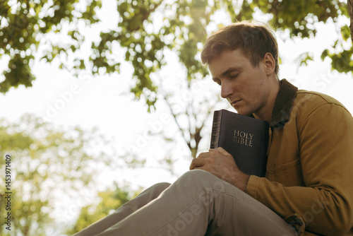 фотографія Young man praying outdoors with Bible in arms