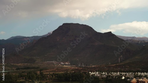 4K Timelapse of a mountain in Tenerife, Spain. The sun is shining on the mountain and clouds moving fast throwing shadows with Chiaroscuro and distant cars driving.  Fixed camera on a tripod 90mm lens