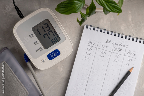 Young woman control blood pressure with BP monitor and records results in notebook.