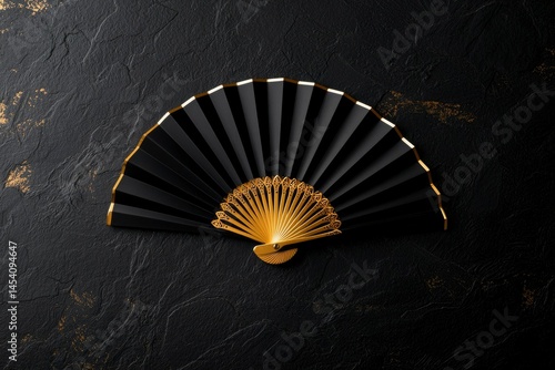 Obraz na płótnie Elegant, black fan with gold accents sits against textured dark surface in an overhead shot w salonie