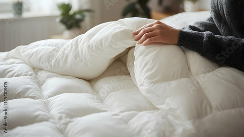 Woman's restful hand upon fluffy white down comforter in serene bedroom setting