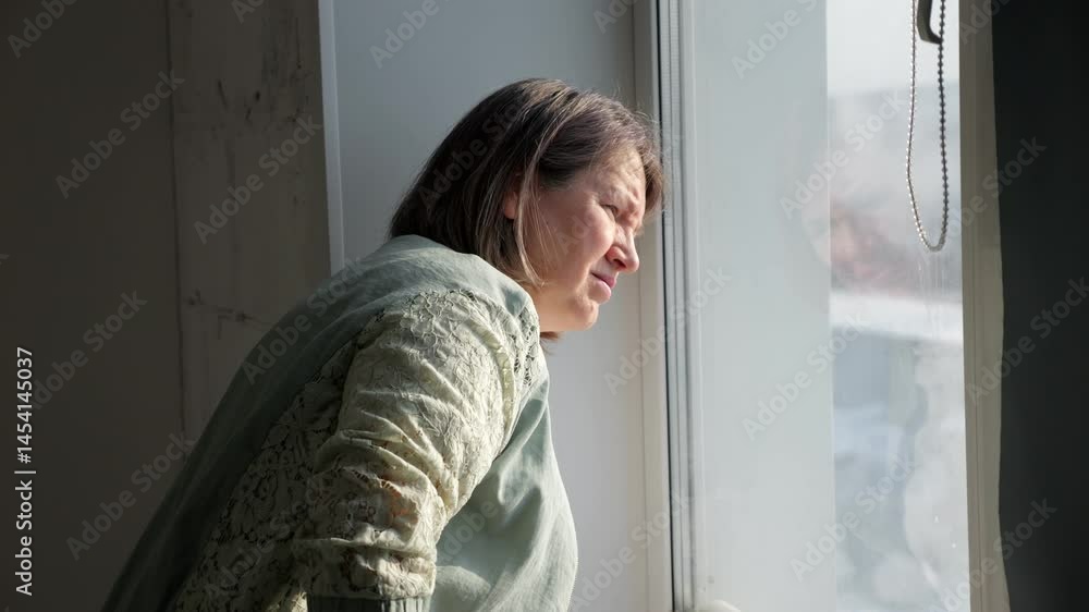 Contemplative woman stands by window looking out and talking Contemplative woman stands by window looking out and talking
