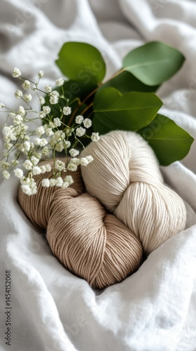 Cozy yarn balls with delicate white flowers and green leaves on soft fabric