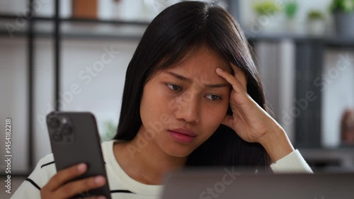Young asian woman sitting at home looking confused and concerned while reading smartphone screen, concept of unexpected news, online problem, or misunderstanding