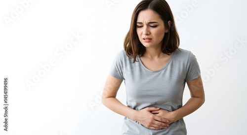 A woman in a gray shirt holds her stomach with a pained expression against a white background space