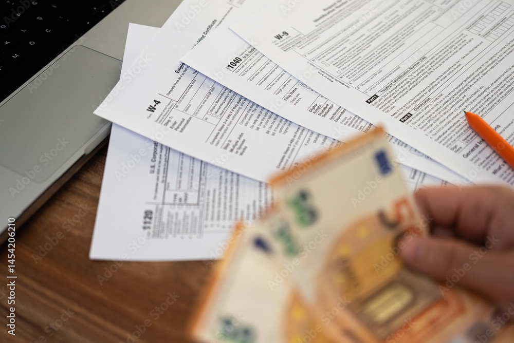 Obraz premium Accountant hand holds euro banknotes preparing financial information for filling various tax forms in compliance with law at workplace with laptop in company office