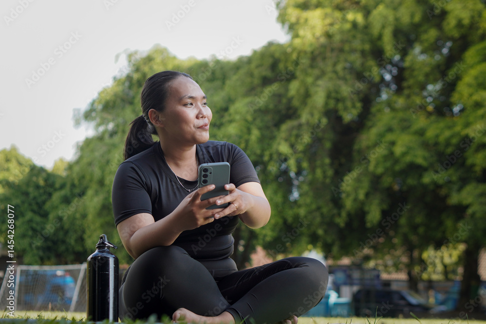 Mindful Asian woman wearing sportswear using smartphone after doing yoga exercise at outdoor public park Mindful Asian woman wearing sportswear using smartphone after doing yoga exercise at outdoor public park