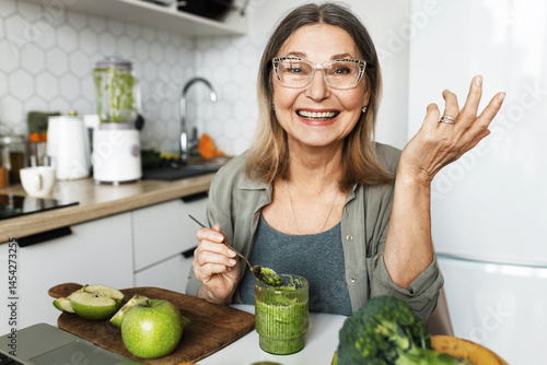 Foto Happy elderly woman having fresh green homemade detox smoothie gesticulating at
