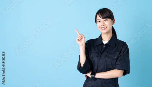 作業着を着た明るく清潔感のある20代の日本人女性、人差し指で説明しているポーズスタジオ撮影風