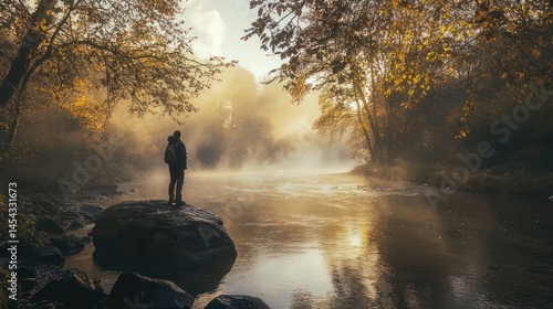 Man standing on a rock near a river, mist hovering over the water, sunshine casting light through foggy trees
