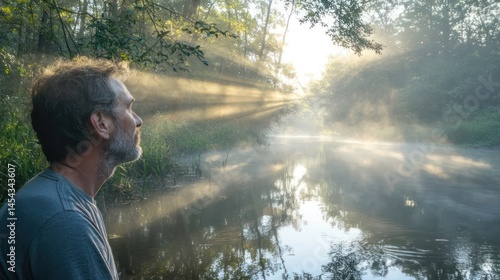Portrait of a man looking out over a forest river, sunbeams filtering through the fog, trees reflecting in the water