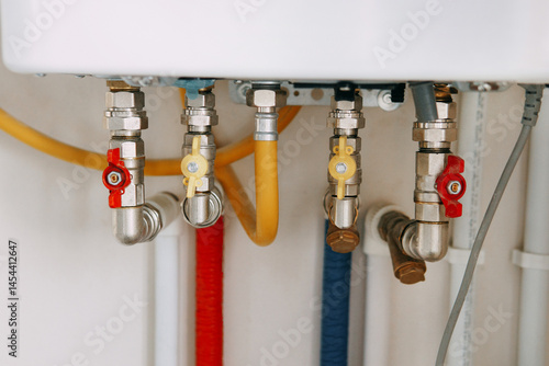 Close-up view of water heater pipes and valves in a utility room, featuring colorful connectors and tubes. Essential components for heating system maintenance and operation. Gas boiler taps.