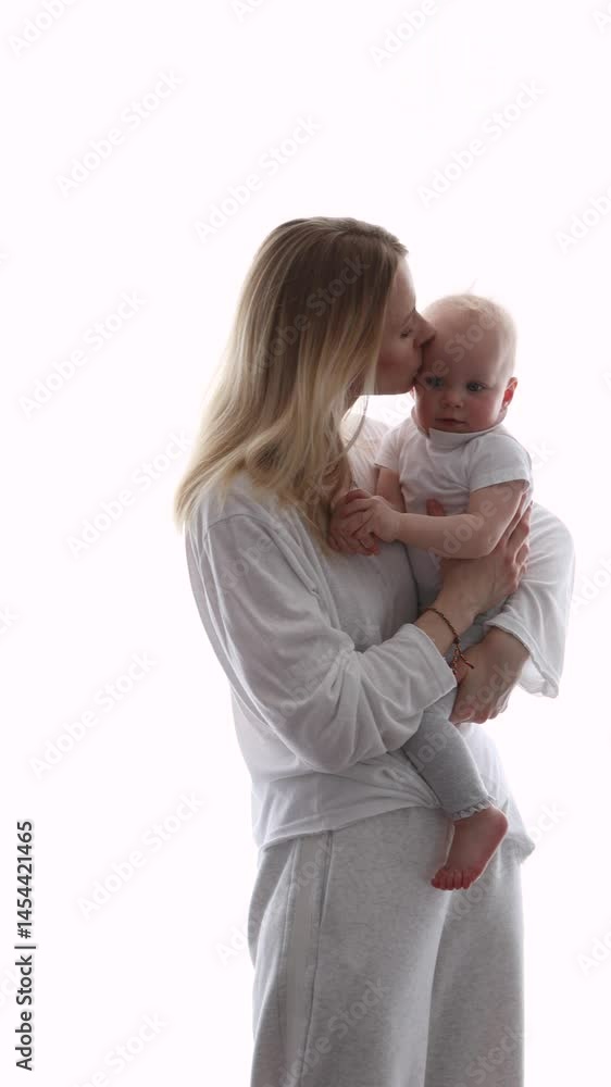 Young mother gently kissing baby while holding child in arms, tender moment of love and care, natural bright light, white background. Mom and Child on Mother's Day