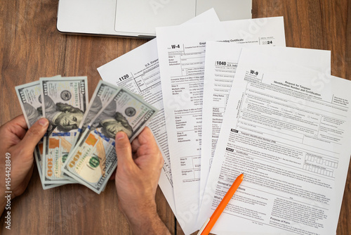 Man freelancer holds cash counting dollar banknotes preparing money for future tax obligations in compliance with law sitting at workplace with tax forms and laptop