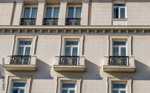 A classic building facade with three ornate balconies and large windows, showcasing elegant architectural details in neutral tones under natural light