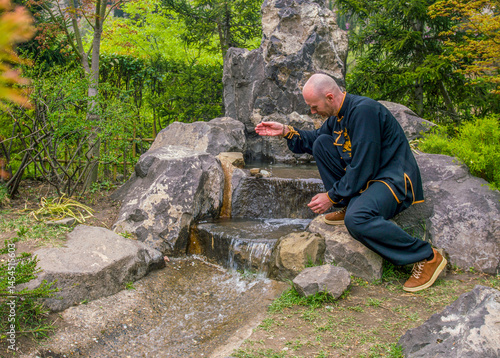 Young man in suit of Chinese (Tibet) buddhist  monastery and source of water in chinese garden (ot Japanese)