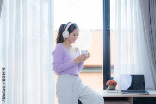 Free Download Young woman wearing headphones is enjoying a cup of coffee in her bright and airy home office, taking a break from work to relax and recharge - GFXLoad