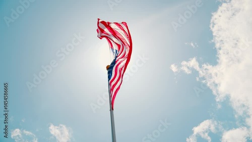 USA flag waiving on the flagpole with a background of the clear blue sky and white cloud.