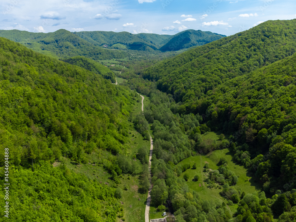 Aerial view of a dirt road between hills with green forests