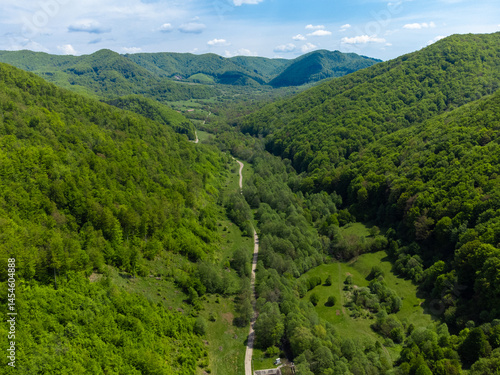 Obraz na płótnie Aerial view of a dirt road between hills with green forests w salonie