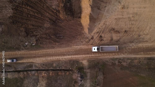 Aerial high angle footage of end dump truck unloading dirt and gravel at a dump site during the construction of a highway.  Top down drone view of  dumping payload after hauling from industrial site.
